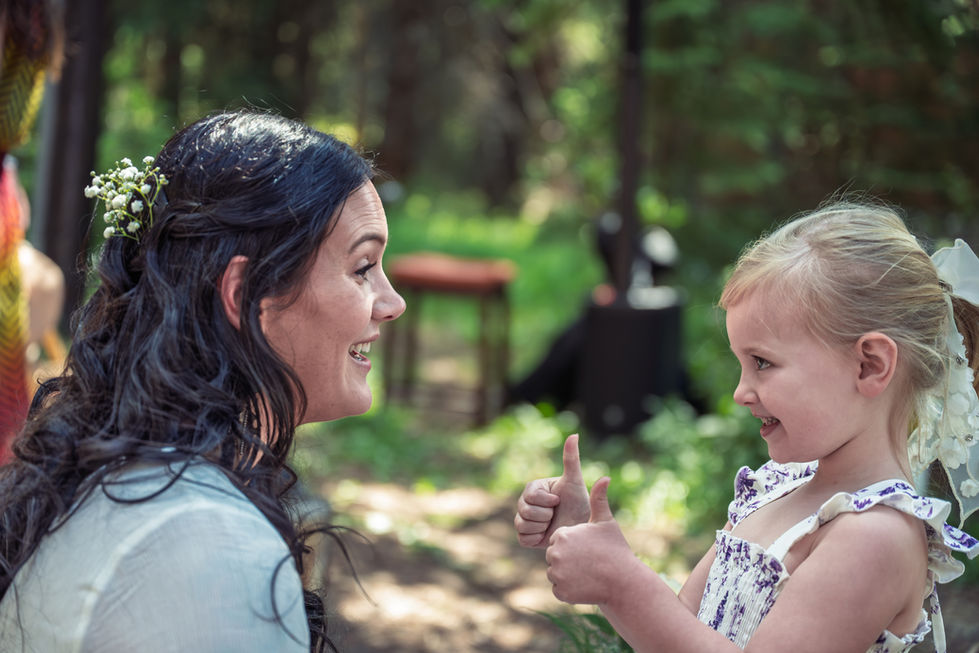 Woman and child smiling outdoors, exchanging thumbs up.