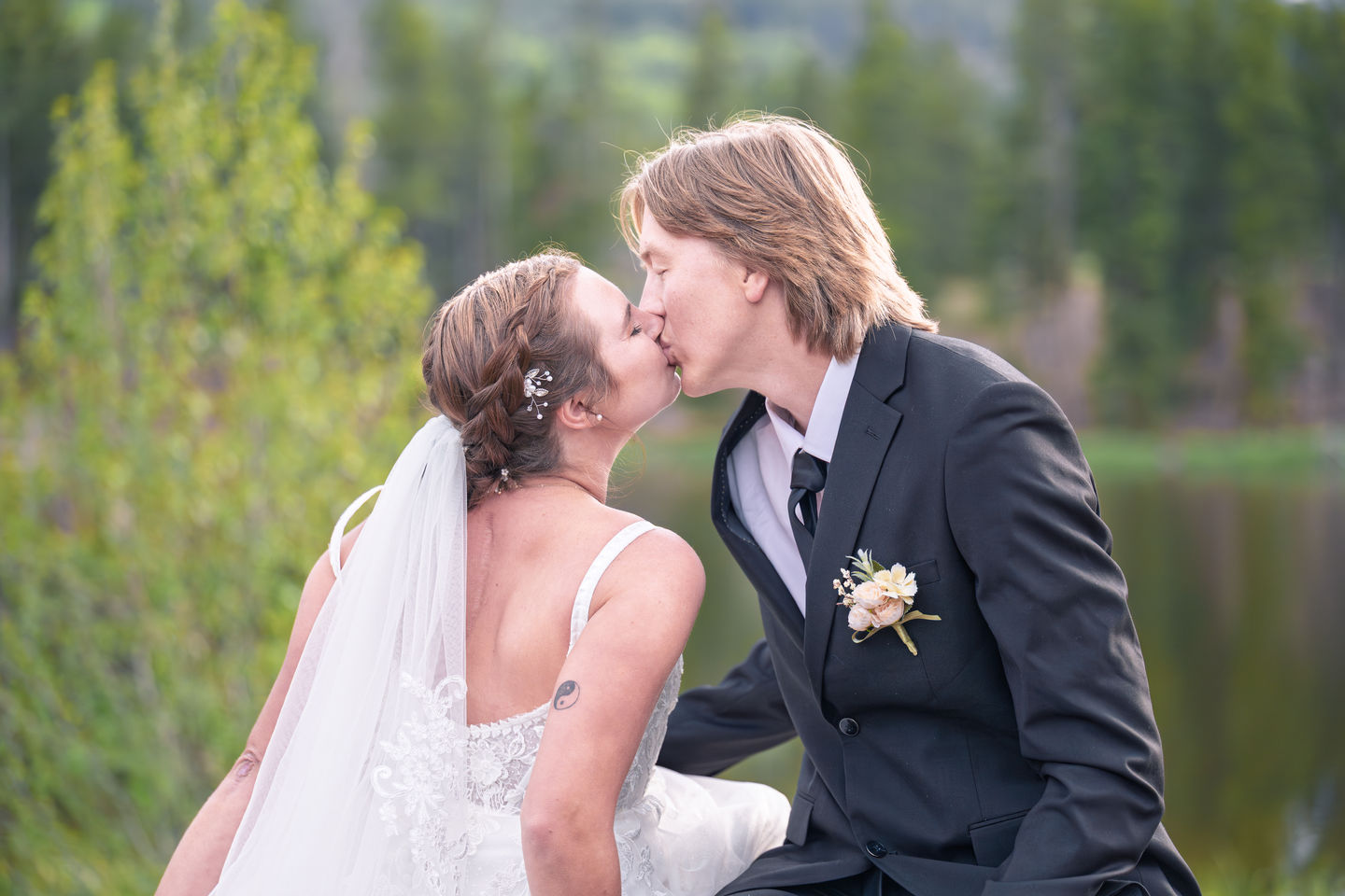 a bride and groom kissing in front of a lake