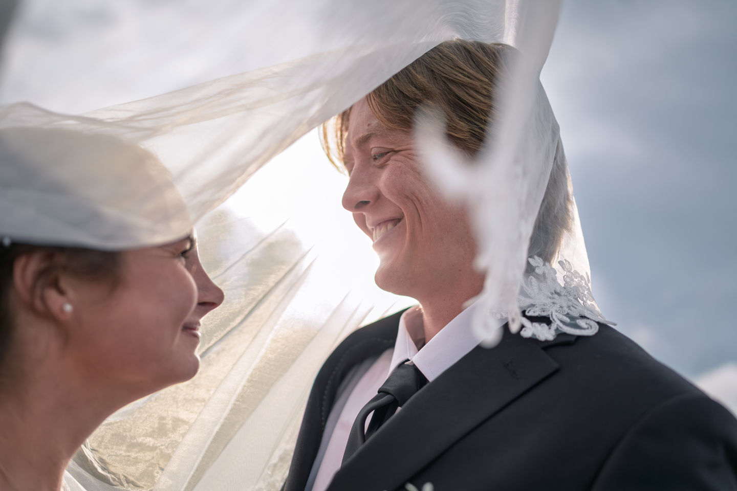 a bride and groom looking at each other with the bride 's veil blowing in the wind