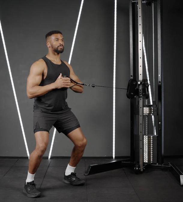 Man in black workout gear performs a cable chest press in a gym with dark walls and white light stripes.