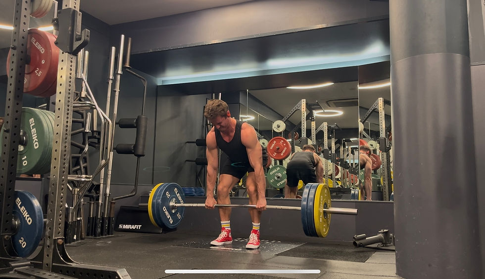 Man in a gym lifting a barbell with colored weight plates. Mirrors reflect his image, and red shoes add a pop of color to the neutral setting.
