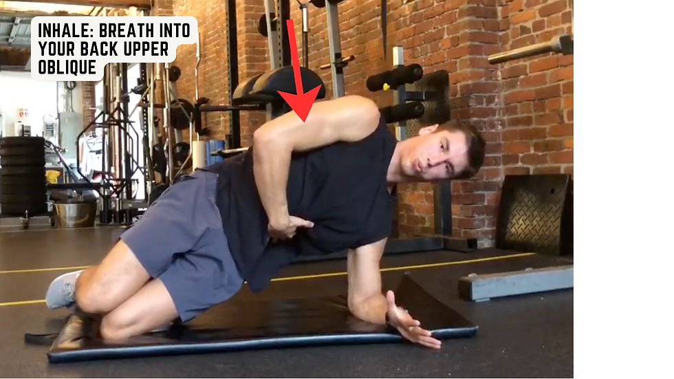 Man kneels on a gym mat doing a side stretch, with a red arrow and text reading INHALE: BREATH INTO YOUR BACK UPPER OBLIQUE.