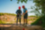 A qualified Rock Climbing Instructor checks the ropes of a participant as they prepare to do an abseil down a cliff.