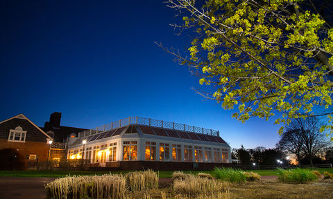 Elegant glass conservatory venue glowing at twilight, surrounded by landscaped grounds and trees