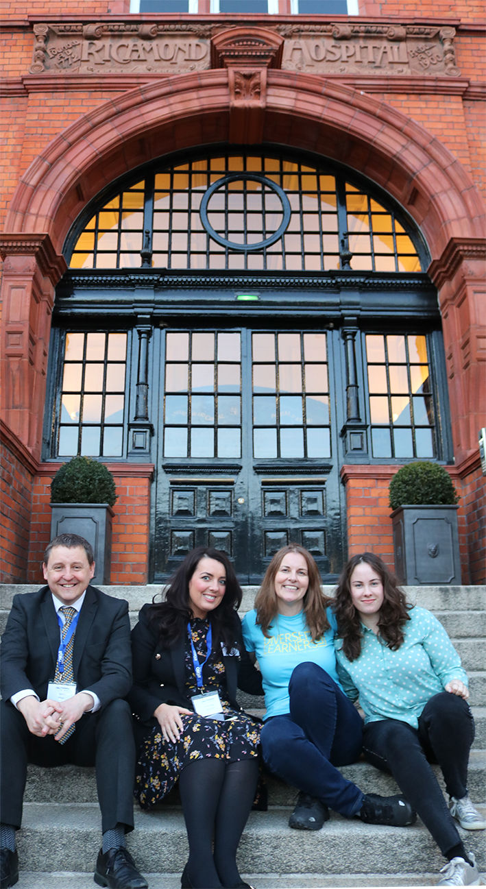 Founder Kerry Pace and three organisation members sitting together on outdoor steps smiling at the camera..