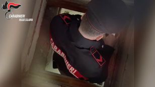 Carabinieri ispezionano l'accesso a un bunker sotterraneo nascosto sotto la botola del pavimento di un casolare rurale