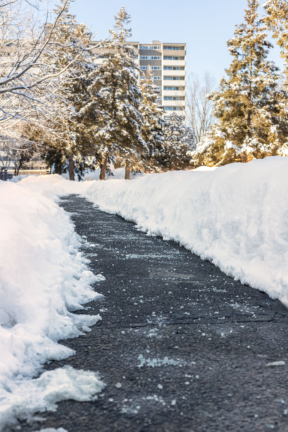 A sidewalk curves through a thick blanket of snow, creating a path flanked by towering snowdrifts.