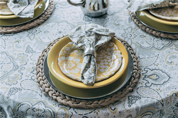 A paisley tablecloth in cheery yellow layers beneath seagrass chargers, yellow plates and coordinating napkins
