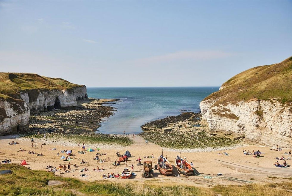 A coastal scene at Thornwick Bay near Bungalow Farm in Buckton, with chalk cliffs, sandy beach, fishing boats and calm blue sea under a clear sky on the Yorkshire coast.