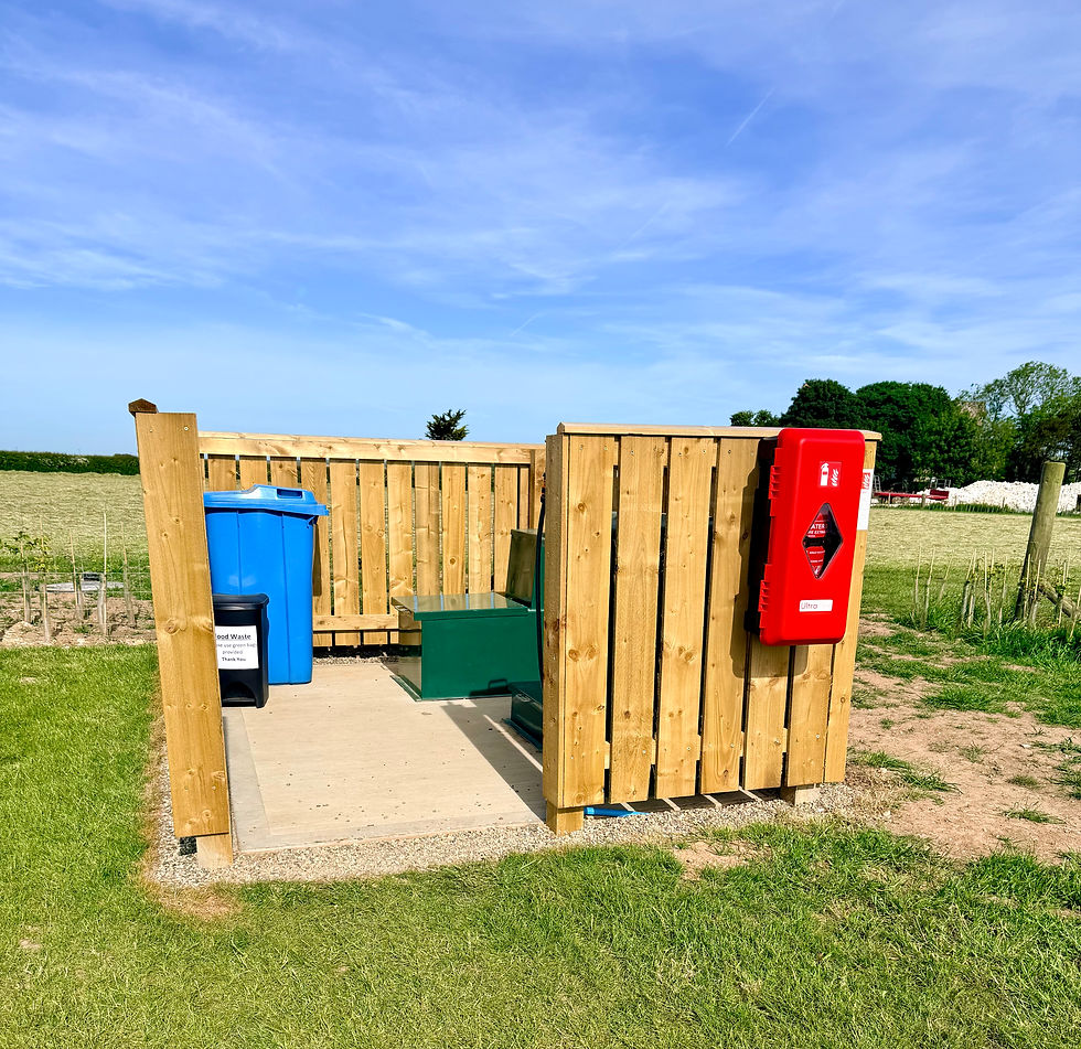 A tidy utility and waste area at Bungalow Farm in Buckton, featuring recycling and general waste bins inside a wooden enclosure with a red emergency box, set against open fields and clear rural views.