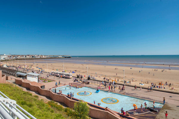 A sunny day at Bridlington South Side Beach near Bungalow Farm in Buckton, with families enjoying the wide sandy beach, shallow play area and bright blue sky along the Yorkshire coast.