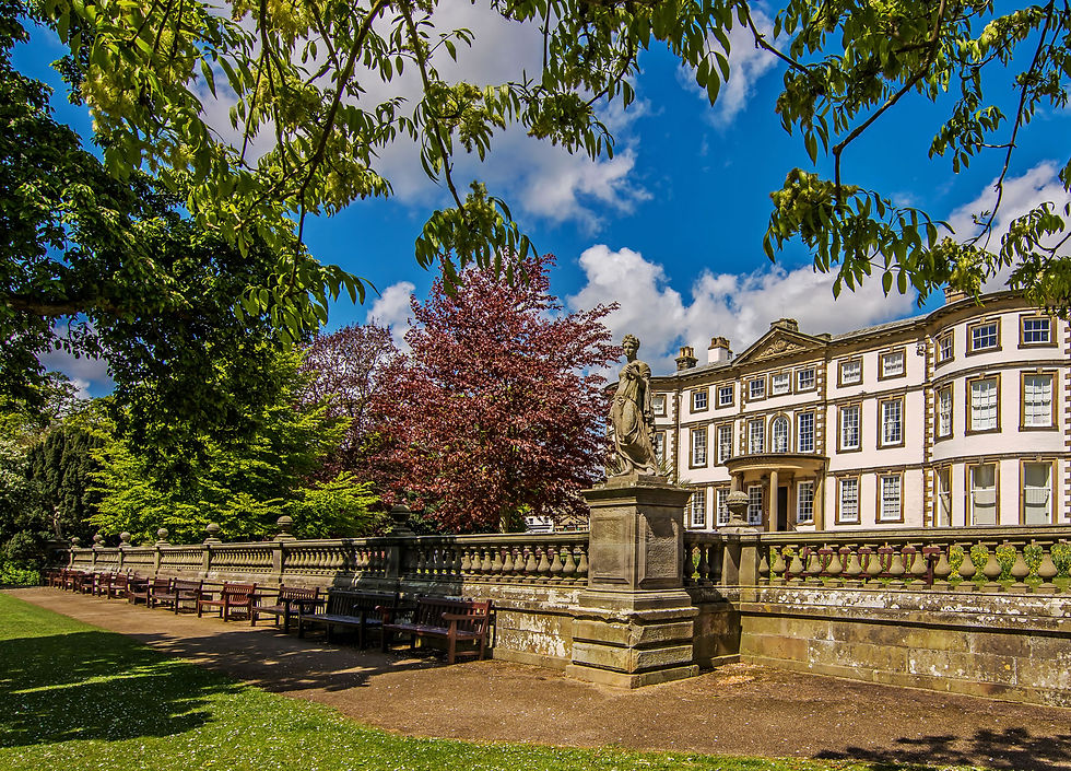 The historic façade of Sewerby Hall near Bungalow Farm in Buckton, with a classical statue, manicured lawns, benches and colourful trees under a bright blue sky.