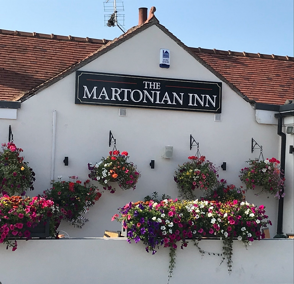 The Martonian Inn near Bungalow Farm in Buckton, a white‑fronted village pub with hanging baskets and vibrant floral displays beneath a tiled roof, creating a colourful and welcoming countryside