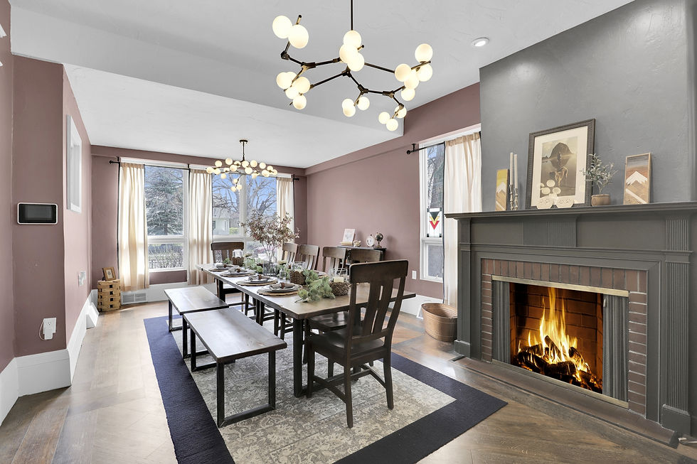 Dining room with a rustic table set for dinner, lit fireplace, framed art on mantel, pastel walls, and a modern chandelier. Cozy ambiance.