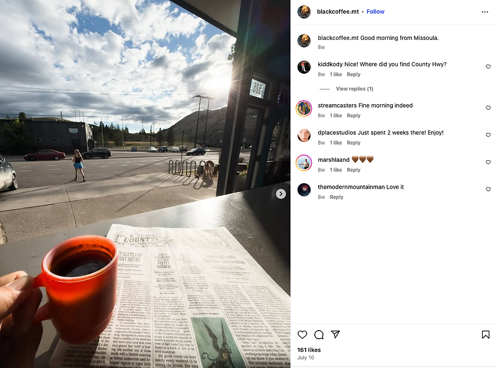 Red mug and newspaper on a table with a street view. A person walks across under a cloudy sky, sunlight filters through, creating a calm vibe.