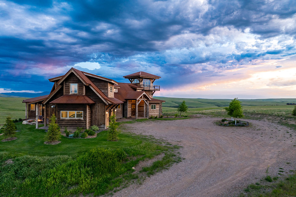Rustic wooden house with red roofs on a vast grassy plain, under a dramatic sunset sky with blue, purple, and pink clouds. Tranquil mood.