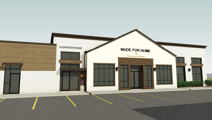 White building with wood accents labeled "MADE FOR HOME by hannesson home." Empty parking lot and plants in front, clear sky backdrop.
