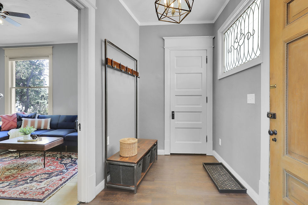 Entryway with gray walls and white doors, bench with baskets, and geometric light. View of a living room with a blue sofa and colorful rug.