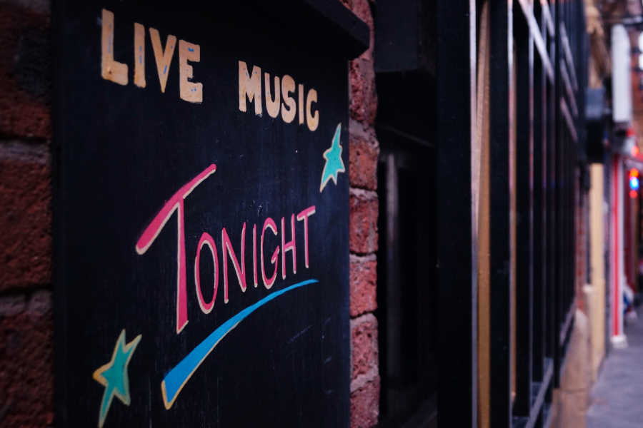 Chalkboard on a brick wall shows "Live Music Tonight" in colorful letters with stars. The lively street is blurred in the background.