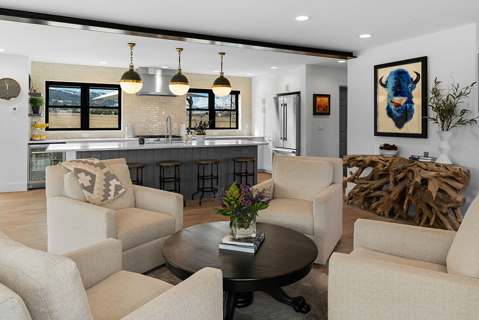 Modern living room with beige chairs, a round table with flowers, and a kitchen in the background. Art of a blue buffalo on the wall.