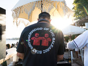 Beach DJ playing at a lively seaside party under a fringed umbrella, with guests mingling on the sand by the ocean.