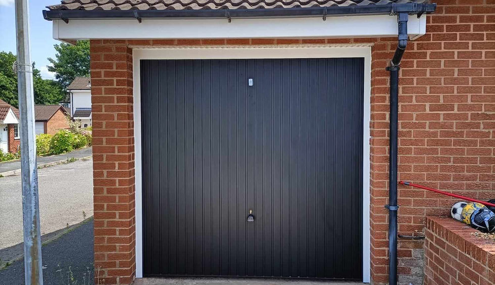 Simple black up and over garage door, on purpose-built garage in brick. Blue sky and clouds.