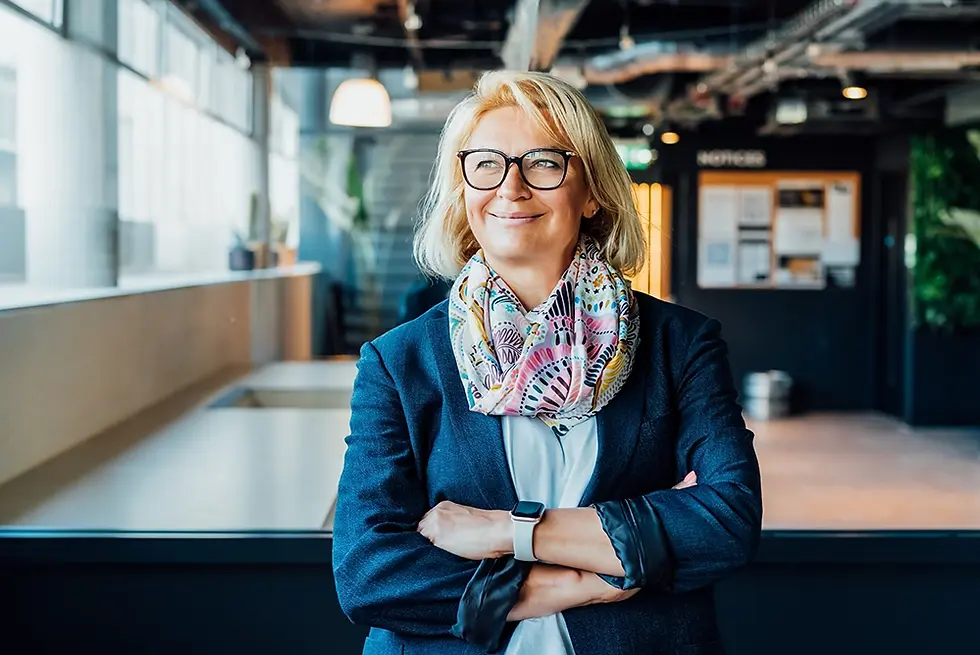 Confident senior female business professional wearing glasses and a navy blazer, smiling with arms crossed in a modern office, representing business leadership, experience and professional expertise.
