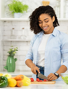 Image of a woman cutting tomatoes in a kitchen with vegetables on the counter.
