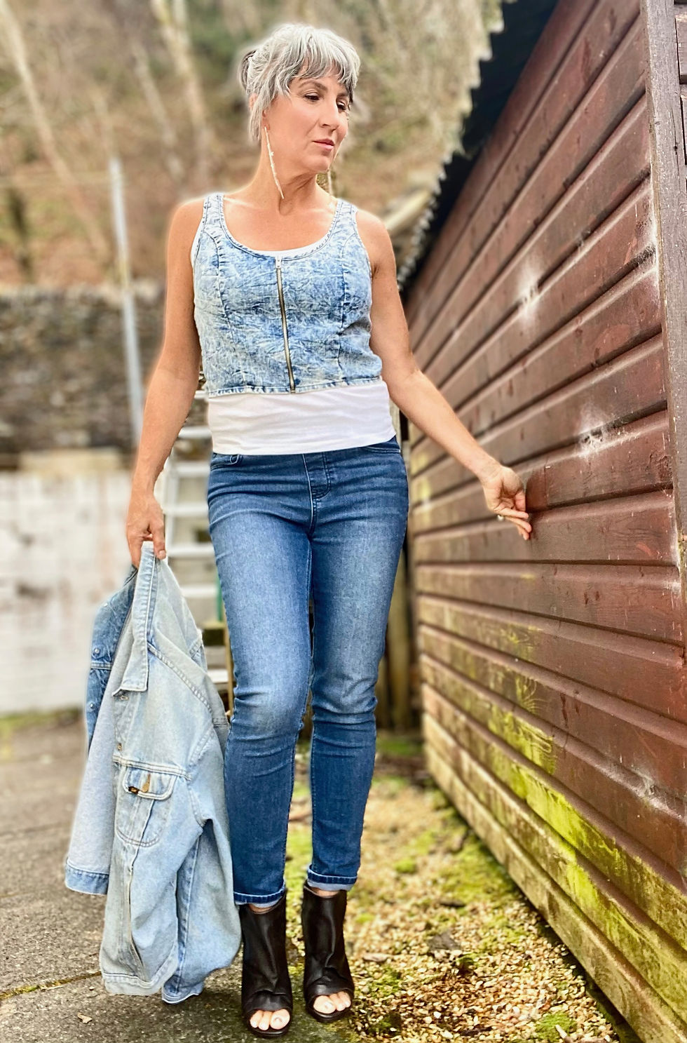 A woman wearing an acid wash denim vest layered over a white tank top