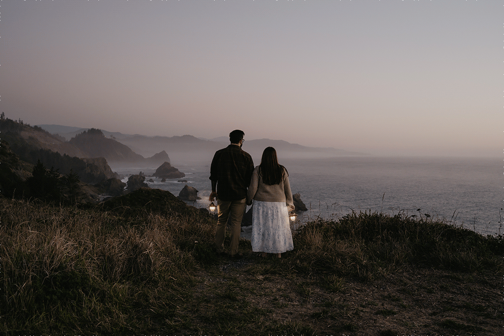 elopement couple holds hands and lanterns on a seaside cliff after sunset