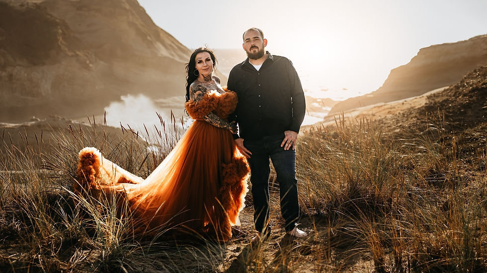 couple in orange and black attire stand on oregon coast cliff at golden hour