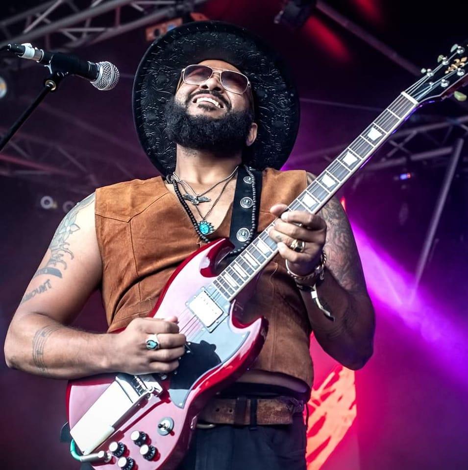 Darnell Cole singing and playing a red SG guitar under magenta stage lights