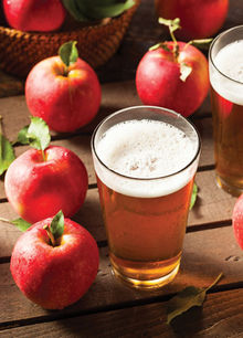 Glass of hard apple cider next to fresh red apples