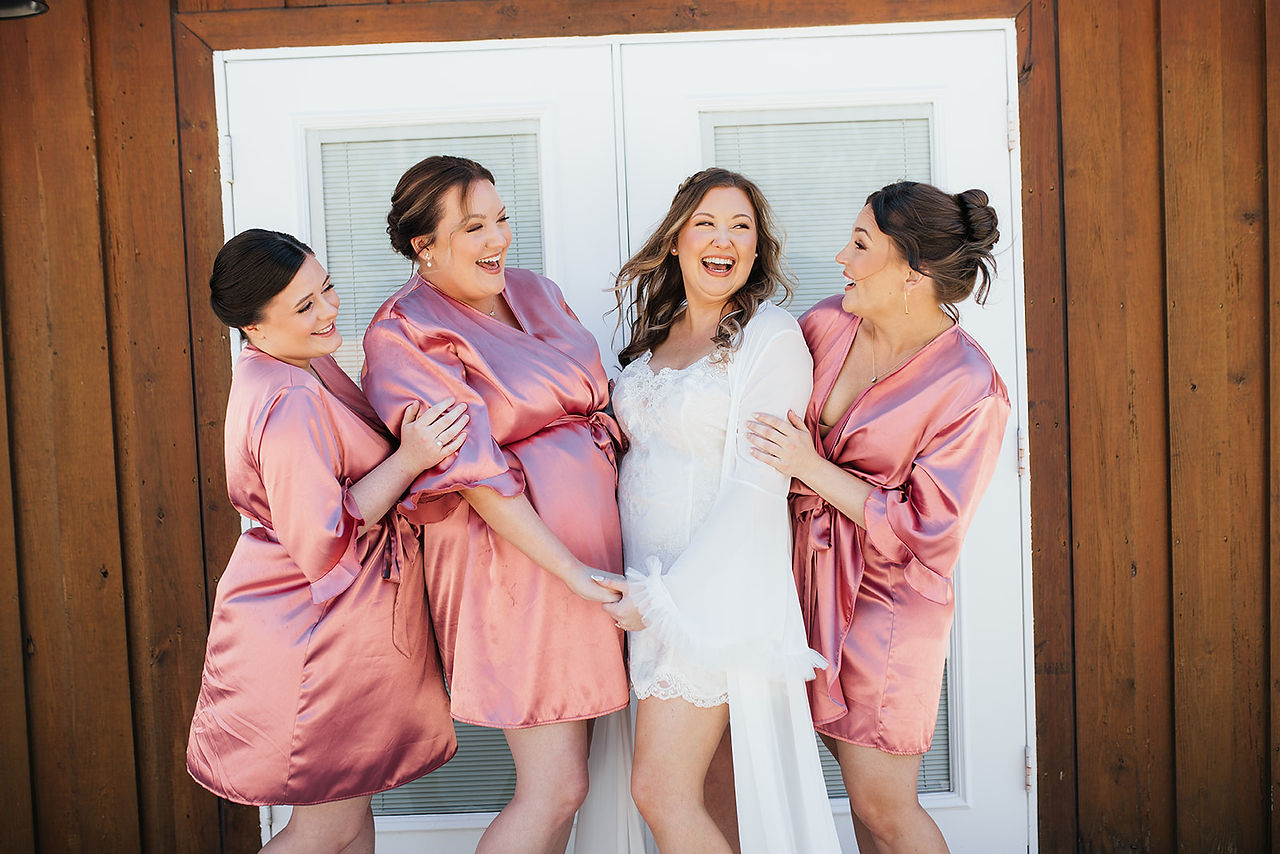 Bride and bridesmaids wearing matching robes, laughing together during getting ready photos in North Florida