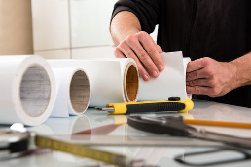 Man's hands with roll of paper on table with other rolls as well as supplies