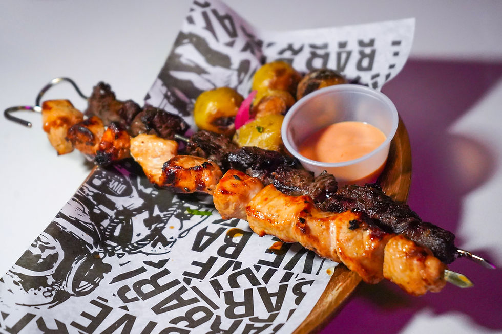 Grilled meat skewers with potatoes and sauce on printed paper. Warm tones and rustic setting create an appetizing presentation.