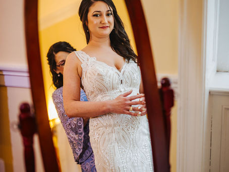 Bride looking at herself in the mirror while her mother adjusts her gown before the ceremony
