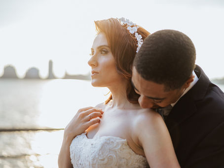 Groom embraces bride from behind at sunset along the NYC waterfront, capturing a quiet moment of calm before their multicultural wedding celebration.