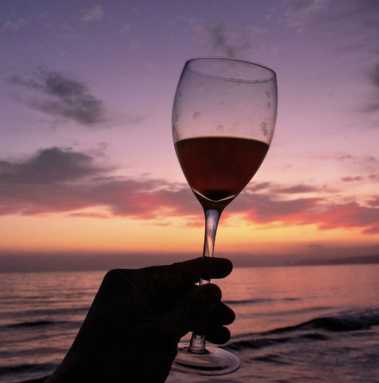 A hand holding a glass of wine against a breathtaking pink and purple sunset.