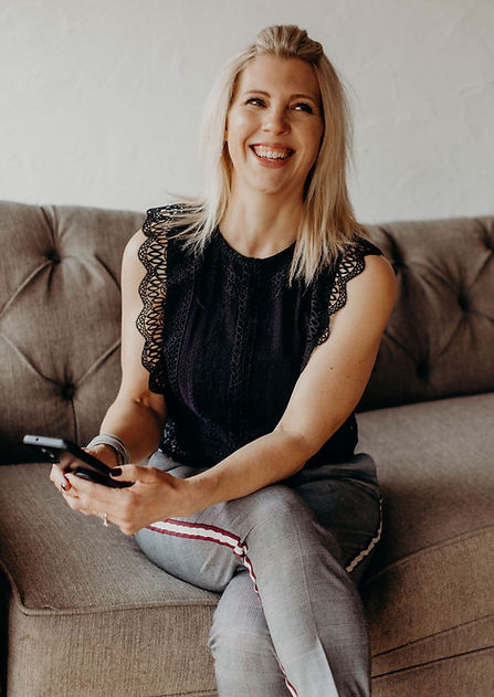 Britt Bilgrien smiling while seated on a sofa, holding a phone — ready to connect with clients. Contact Bilgrien Health