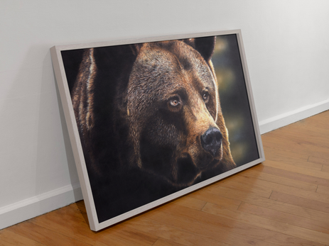 ‘Out of Darkness,’ bear artwork in a light brown frame, leaning against a wall on a wooden floor.