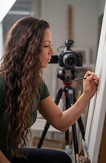 Artist working in the studio beside a camera and canvas, showing the focused process behind hyperreal artwork.