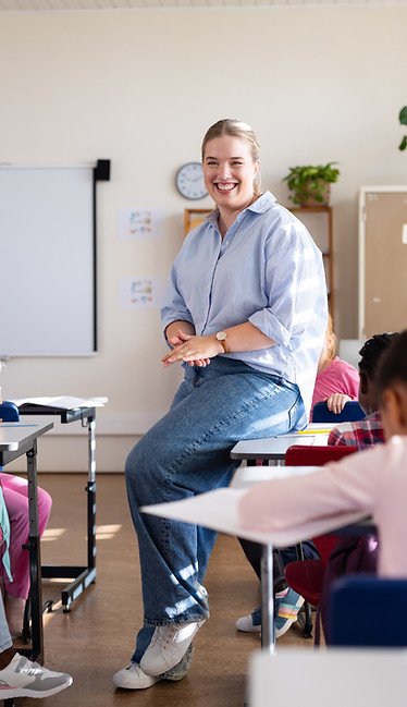 In school, female teacher smiling and engaging with diverse students in classroom setting.