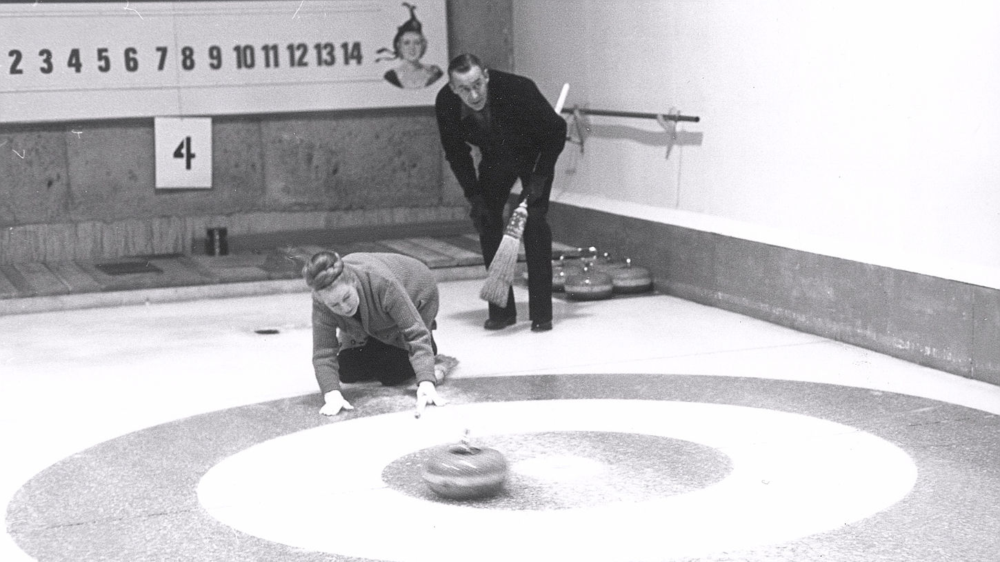 A man and a woman curling on the ice rink