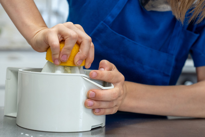 Child squeezing a lemon on a white citrus juicer for fresh juice.