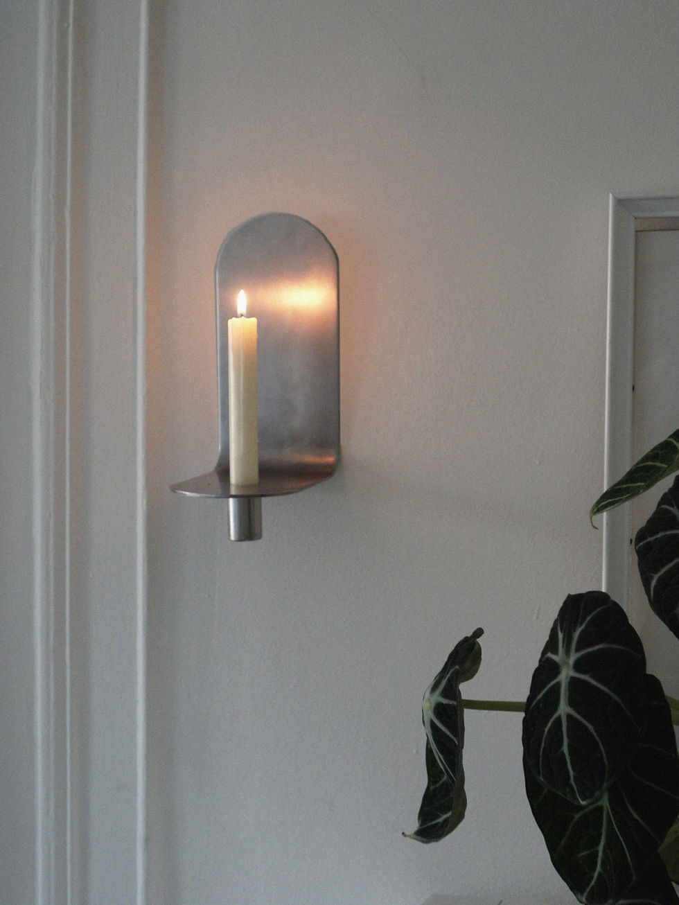 Side view of a contemporary brushed steel candle holder with a white taper candle.