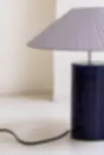 Close-up of a handcrafted ceramic table lamp featuring a deep blue glazed ceramic base and elegant pleated fabric shade