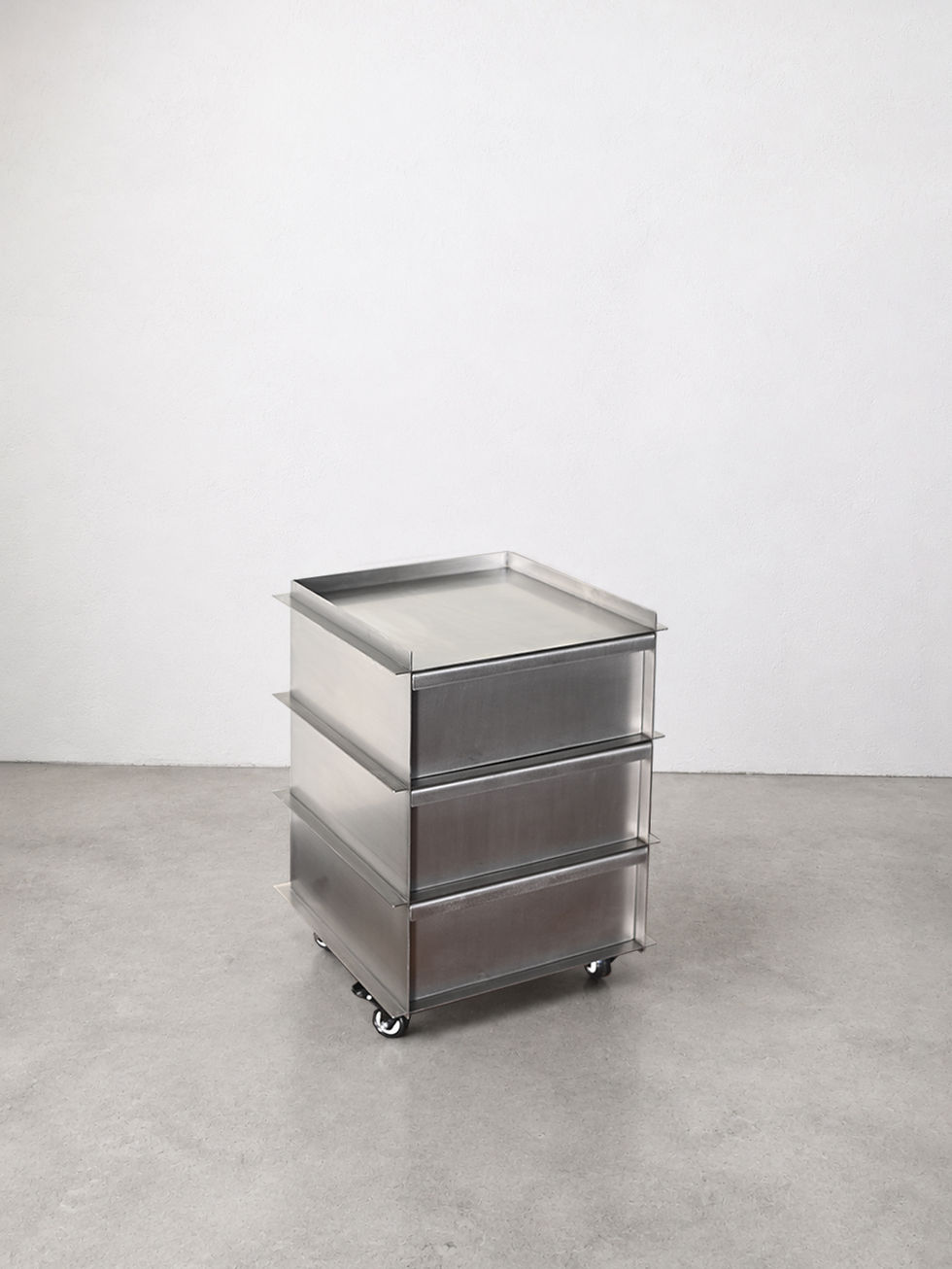 Three brushed stainless steel mobile drawer cabinets with partially open drawers on a wooden floor.