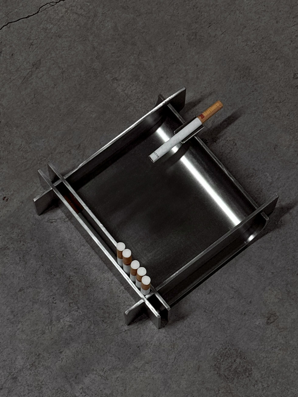 Minimalist stainless steel ashtray placed on a raw concrete floor with cigarettes stored in the integrated holder