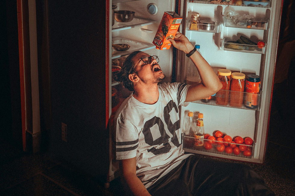 A man with glasses sitting in front of an open fridge holding up an empty carton.